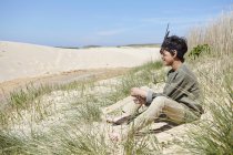 Young boy, wearing fancy dress, sitting on sand dunes — Stock Photo