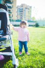 Femme tout-petit tenant sur poussette dans le parc — Photo de stock