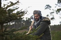 Junger Mann hackt Weihnachtsbaum im Wald — Stockfoto