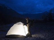 Homme par tente illuminé la nuit, Premosello, Verbania, Piedmonte, Italie — Photo de stock