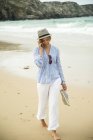 Donna matura che chatta sullo smartphone mentre passeggia sulla spiaggia, Camaret-sur-mer, Bretagna, Francia — Foto stock