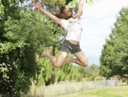 Teenage girl jumping with arms outstretched, mid-air, outdoors — Stock Photo