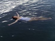 Високий кут зору жінки, що плаває на спині у водяних обіймах, витягнутих, дивлячись вгору — стокове фото