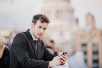 Homem de negócios enviando mensagens no smartphone enquanto se inclina na ponte Millennium, Londres, Reino Unido — Fotografia de Stock