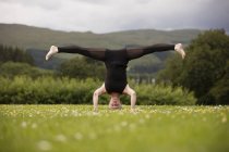 Зріла жінка практикує йогу стоячи на голові з відкритими ногами в полі — стокове фото