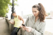 Two runners texting on smartphone at riverside — Stock Photo