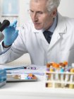 Doctor looking at patients blood slide under microscope with other samples for testing — Stock Photo