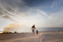Зрелый мужчина прогуливается со своей маленькой дочерью на пляже на закате, Кальви, Корсика, Франция — стоковое фото