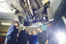 Five college students looking up from beneath car in garage workshop — Stock Photo