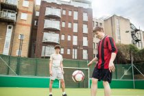 Dos jóvenes jugando al fútbol en el campo de fútbol urbano - foto de stock