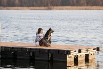 Mitte erwachsene Frau und ihr Hund sitzen auf Seebrücke — Stockfoto