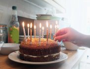 Hand of young woman placing lit candles on birthday cake — Stock Photo