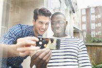 Two young male friends taking selfie behind patio glass — Stock Photo