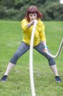 Junge Frau zieht Seil auf Feld — Stockfoto