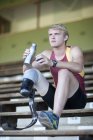 Sprinter sitting with prosthetic leg on and drinking water — Stock Photo