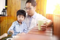 Chinese father and young son having breakfast on the balcony in the sunshine together — Stock Photo