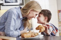 Boy holding croissant, face to face with mother — Stock Photo