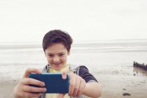 Un adolescent souriant prend un selfie smartphone au bord de la mer, Southend on Sea, Essex, Royaume-Uni — Photo de stock