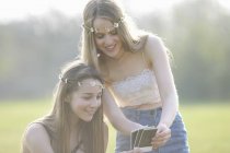 Две девочки-подростки в платьях из маргаритки смотрят на фотографии в парке — стоковое фото