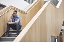 Молодой бизнесмен сидит на служебной лестнице и болтает на смартфоне — стоковое фото