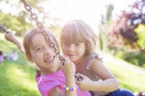 Portrait of two young girls swinging together on park swing — Stock Photo