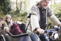 Mature hippy couple riding tricycle and trailer on rural road — Stock Photo