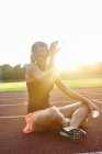 Young female runner cross legged on race track drinking water — Stock Photo