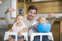 Father pointing at male and female twin toddlers in high chairs — Stock Photo