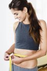 Sorrindo jovem mulher medindo sua cintura com fita métrica — Fotografia de Stock