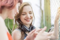 Young women using smartphone beside fence — Stock Photo