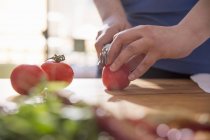 Abgeschnittenes Bild einer Frau, die Tomaten am Küchentisch schneidet — Stockfoto
