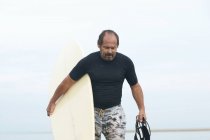 Surfeur portant une planche de surf sur la plage — Photo de stock