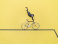 Ciclista urbano fazendo acrobacias ilusórias contra a parede amarela — Fotografia de Stock