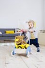 Menino empurrando carrinho de brinquedos em casa — Fotografia de Stock