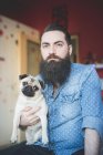 Молодий бородатий чоловік носить собаку на руках — стокове фото