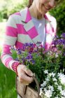 Reife Frau trägt gestreifte Jacke mit einer Holzkiste voller Blumen und lächelt — Stockfoto