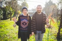 Пара стоящих в саду со свежими луковицами чеснока, смотрящих в камеру улыбающихся — стоковое фото