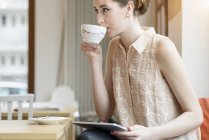 Молода бізнес-леді в кафе п'є каву і використовує цифровий планшет — стокове фото