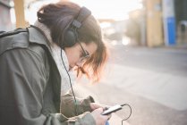 Молода жінка сидить на тротуарі читаючи тексти смартфона — стокове фото