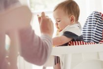 Mother feeding baby boy in baby chair — Stock Photo