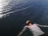 High angle view of young man floating on back in water arms outstretched looking up — Stock Photo