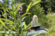 Chica joven sentada en un entorno rural con cuaderno de bocetos - foto de stock