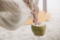 Чоловік насолоджується кокосовою водою в гамаку на пляжі — стокове фото