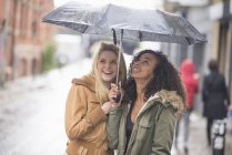 Молоді жінки ховаються під парасолькою на вулиці — стокове фото