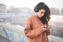 Молода жінка в навушниках вибирає музику на смартфон — стокове фото