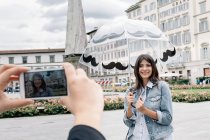 Молода жінка тримає парасольку позують для одного за допомогою смартфона взяти фотографію, площі Санта-Марія-Новелла, Флоренції, Тоскана, Італія — стокове фото