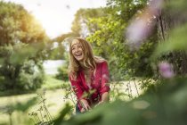 Молода жінка, сміючись в той час як різання квіти в саду — стокове фото