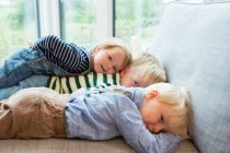Портрет уставшего мальчика и двух малышей, лежащих на диване — стоковое фото