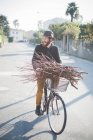 Young man carrying bunch of sticks on bike — Stock Photo
