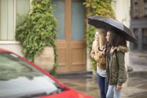 Young women using umbrella on city street — Stock Photo